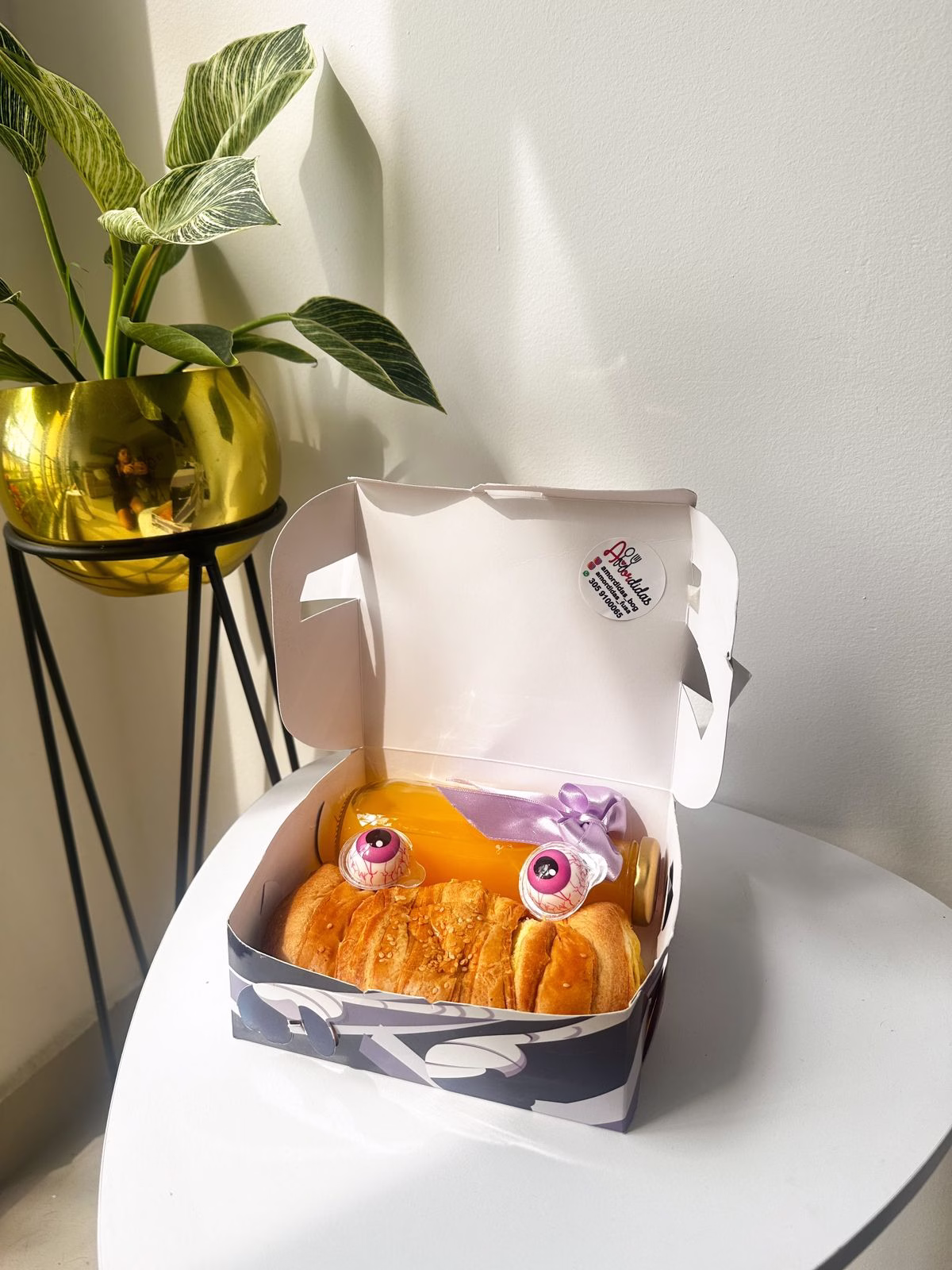 Cajita Halloween empresarial con croissant, masmelos de ojo y jugo de naranja. - Amordidas